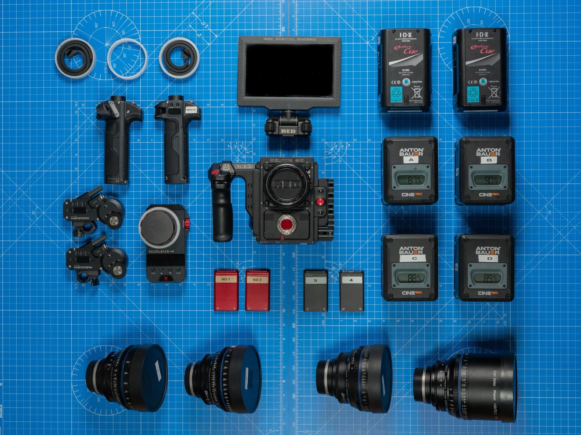 Professional camera rental equipment laid out, including a cinema camera, lenses, batteries and follow-focus accessories