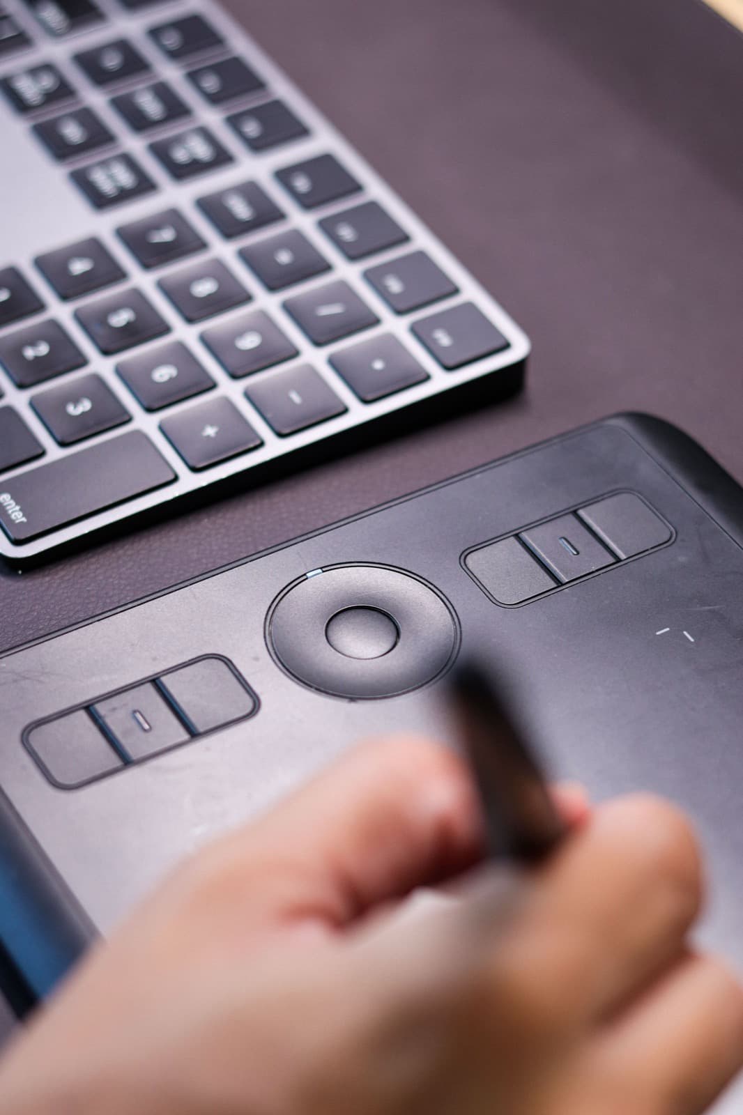 Hand using a stylus on a graphics tablet next to a keyboard
